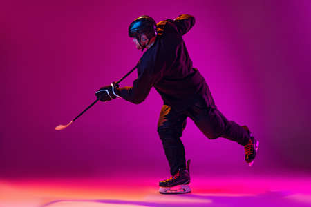 Portrait of professional male hockey player training isolated over pink background in neon.の写真素材