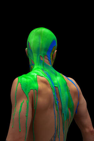 Back view. Portrait of young man being covered with green and blue thick paint flowing down his head and shoulders isolated over black backgroundの写真素材