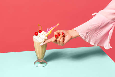 Coffee and whipped cream. Female hand touching high glass with irish coffee isolated on light pink background. Trendy colors. Pop art, retro style.の写真素材