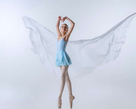 One young girl, aspiring ballerina in blue dress and pointes dancing with cloth isolated on gray background. Art, grace, beauty, ballet school conceptの写真素材