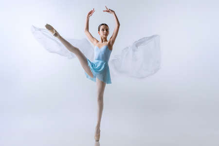 One young girl, aspiring ballerina in blue dress and pointes dancing with cloth isolated on gray background. Art, grace, beauty, ballet school conceptの写真素材