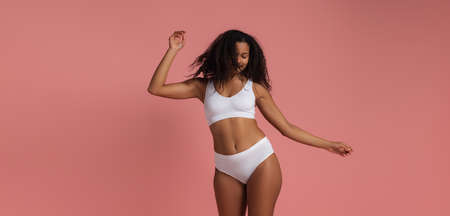 Portrait of cheerful young woman in white underwear posing dancing isolated over pink studio backgroundの写真素材