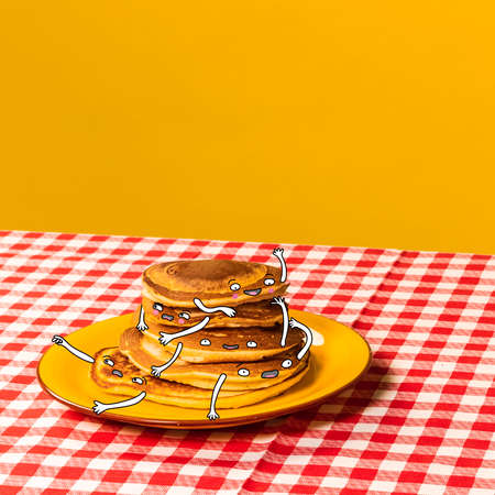 Food pop art photography. Plate with pancakes with funny drawings on plaid tablecloth isolated on bright yellow background. Cartoon, vintage, retro styleの写真素材