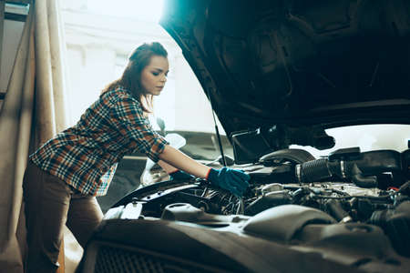 Car reapir, exam. Young pretty girl, auto mechanic working at auto service station using different...