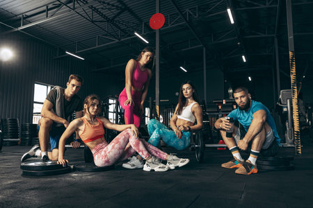 Group of young friends doing sports, training at gym indoors. Cooling down, resting, posing