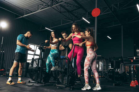 Group of young friends doing sports, training at gym indoors. Woman training at exercise bikeの写真素材