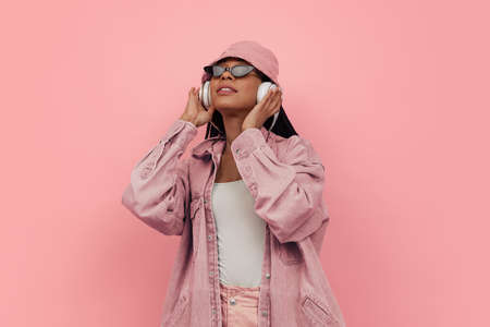 Monochrome portrait of young attractive happy woman in casual style outfit listening to music isolated on pink background. Concept of beauty, art, fashion, youth, styleの写真素材