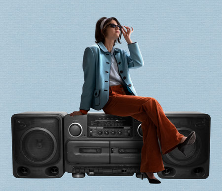 Young stylish woman dressed in 70s, 80s fashion style sitting on vintage record player on blue...