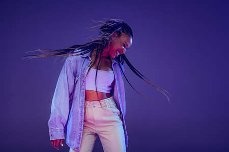 Emotional african girl in jeans and shirt dancing, having fun isolated on dark blue background....
