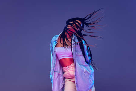 Emotional african girl in jeans and shirt dancing, having fun isolated on dark blue background....