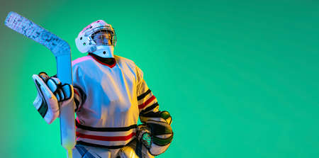 Portrait of boy, child, hockey player in uniform of goalkeeper posing isolated over green background in neon lightの写真素材
