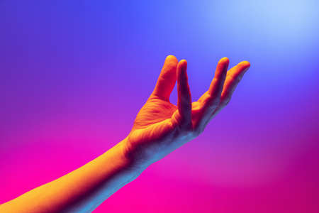 Human hand gesturing isolated on gradient purple-pink background in neon light. Concept of sign language, creativity, symbolism, culture and artの写真素材