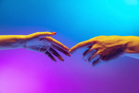 Two human hands touch each other isolated on gradient blue-purple background in neon light. Concept of human relation, togetherness, symbolism, culture and historyの写真素材