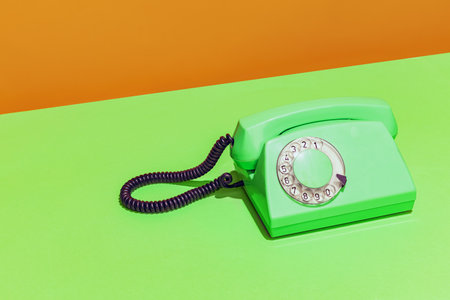 Colorful bright image of green neon retro telephone on light green and orange backgroundの写真素材