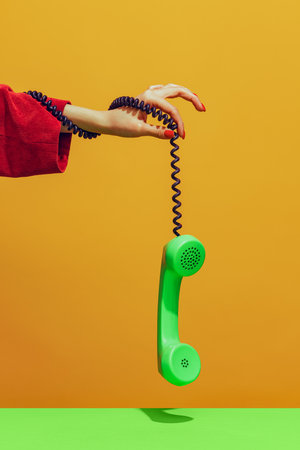 Colorful bright image of female hand holding old-fashioned green colored phone, handset isolated over yellow backgroundの写真素材