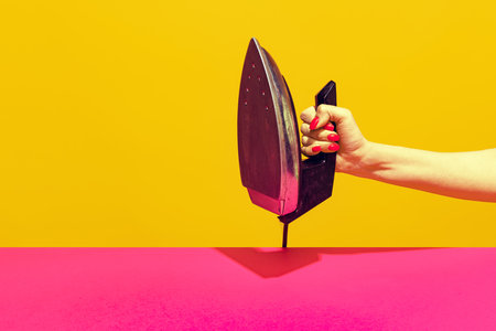 Colorful bright image of female hand holding retro iron isolated over pink yellow backgroundの写真素材