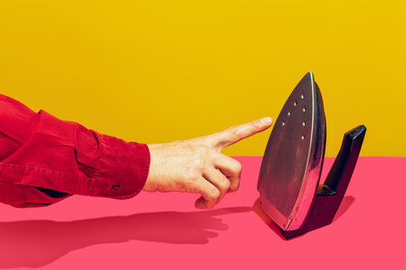 Colorful bright image of male finger touching retro iron isolated over pink yellow backgroundの写真素材