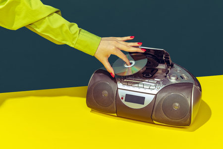 Colorful image of vintage radio player on bright yellow tablecloth isolated over dark green background. Putting music diskの写真素材