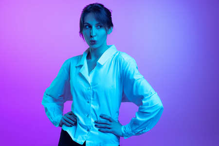 Portrait of pretty young girl in white shirt isolated over purple studio background in neon light. Concept of emotions, facial expression, art, beautyの写真素材