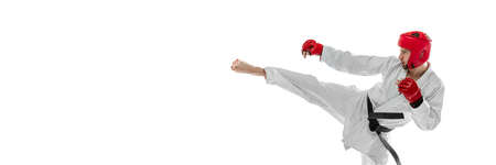 Portrait of young sportive man wearing white dobok, helmet and gloves practicing isolated over white background. Concept of sport, workout, health.の写真素材