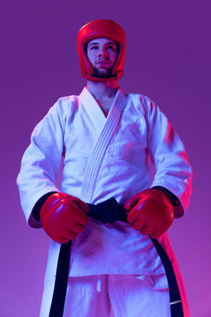 Portriat of male taekwondo fighter in sports uniform posing isolated over purple background in neon light. Concept of sport, workout, competition, adの写真素材