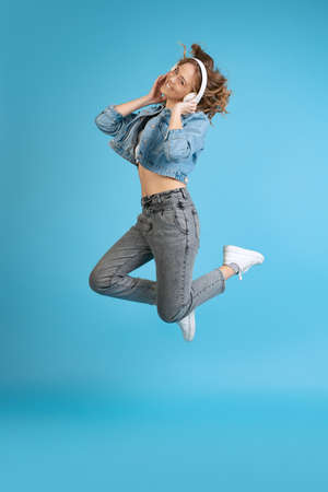 Portrait of young excited girl listening to music in headphones isolated on blue background. Concept of beauty, music, fashion, youth, spring collectionの写真素材
