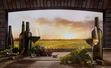 Still life with wine glasses, bottles, grapes on wooden table in wine cellar. Panoramic window view...