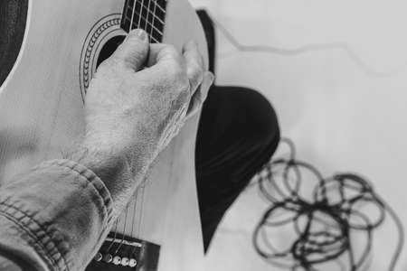 Close-up hands and acoustic guitar. Cropped monochrome portrait of man, rock musician playing guitar isolated on light background. Concept of music, style, artの写真素材