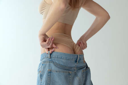Cropped image of woman in underwear putting jeans isolated over grey studio background. Tonned...
