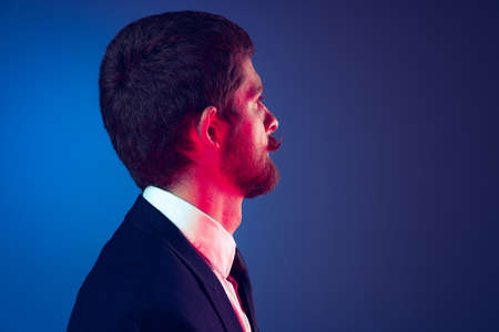 Closeup. Profile view of young stylish bearded man in business suit posing isolated on dark blue...