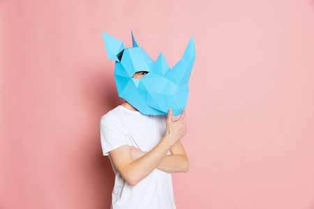 Creative portrait of young man in white t-shirt with cardboard animal mask on his head isolated on pink background. Concept of art, fashion, theater, funny meme emotions.の写真素材