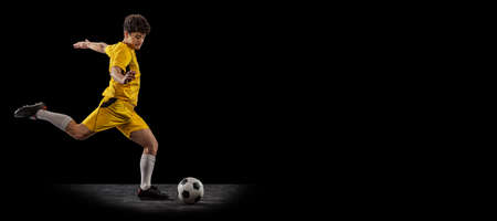 Dynamic portrait of professional football, soccer player training with ball isolated on dark background. Concept of sport, match, active lifestyle, goal and hobbyの写真素材