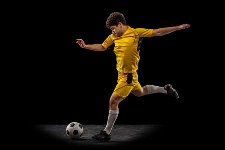 Dynamic portrait of professional football, soccer player training with ball isolated on dark background. Concept of sport, match, active lifestyle, goal and hobbyの写真素材