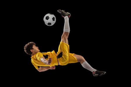 Dynamic portrait of professional football, soccer player training with ball isolated on dark background. Concept of sport, match, active lifestyle, goal and hobbyの写真素材