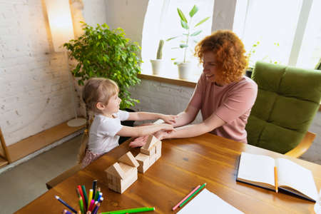 Happy kind woman and cute little girl, mother and daughter playing with wooden toy cubes at home....
