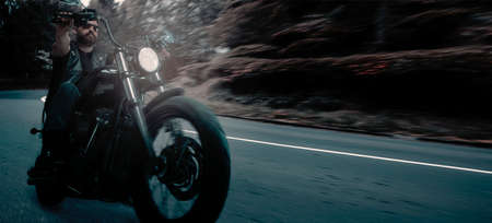 Serious brutal biker riding motorbike in speed highway in summer evening time. Vintage cinematic background and dramatic cloudy sky. Concept of fashion, style and hobbyの写真素材