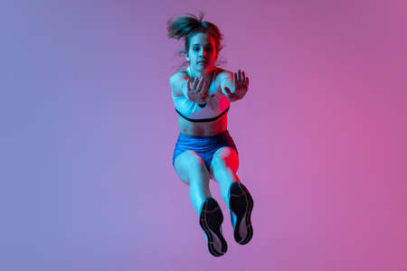 Training in long jump sport. Young girl, female athlete practicing isolated on pink studio background with blue neon filter, light. Concept of action, motion, speedの写真素材