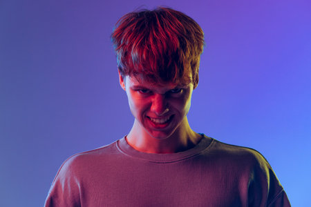 Closeup young red-headed man, student isolated over blue studio background in neon light. Concept of...