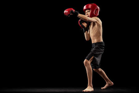 Studio shot of preschool boy, cute kid in sports shots and gloves training alone on black background. Sport, education, action, motion concept.の写真素材