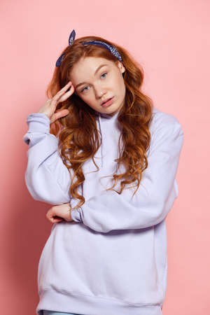 Sad young redhead girl, student posing isolated on pink studio background. Human emotions, facial...
