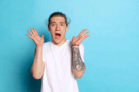 Shocked, surprised young emotional man with long curly hair shouting isolated on blue background. Human emotions, facial expression concept. Trendy colorsの写真素材