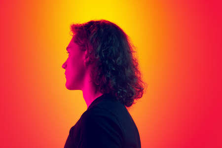 Back view of serious man with long curly hair posing isolated on gradient yellow-magenta background in neon. Concept of beauty, fashion, youth culture and emotionsの写真素材