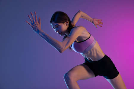 One young muscular girl, female runner or jogger training isolated on pink-blue background in neon light. Sport, track-and-field athletics, competition and active lifestyle conceptの写真素材