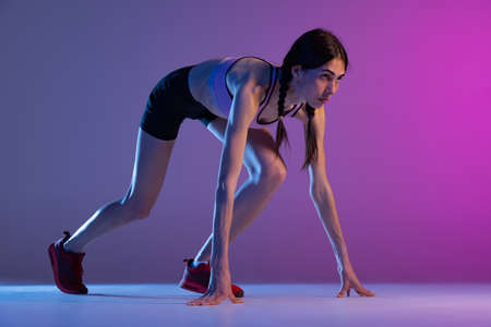 One young muscular girl, female runner or jogger training isolated on pink-blue background in neon light. Sport, track-and-field athletics, competition and active lifestyle conceptの写真素材