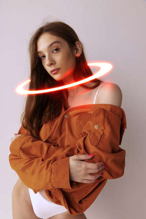 Tender young woman with white neon circle around her neck isolated over light grey background....