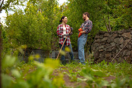Young and happy farmers couple at their garden in sunny day. Man and woman engaged in the...