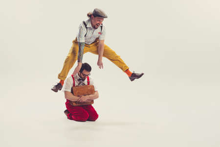 Two cheerfull dudes, young men in old-school fashioned attire running, jumping, having fun isolated on white background. Vintage, retro style conceptの写真素材