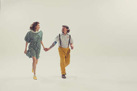Delighted young man and woman in vintage retro style outfits running isolated on white background....