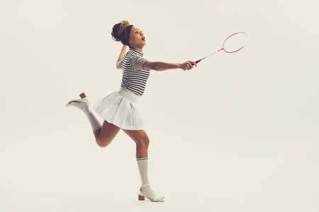 Portrait of young happy beautiful woman in retro, 70s, 80s fashion style clothes, vintage outfit playing badminton isolated on white background. Concept of art, fashion, beauty, sportの写真素材