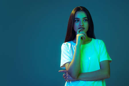 Young beautiful girl with long hair thinking isolated on blue background in neon light. Concept of beauty, art, fashion, emotionsの写真素材